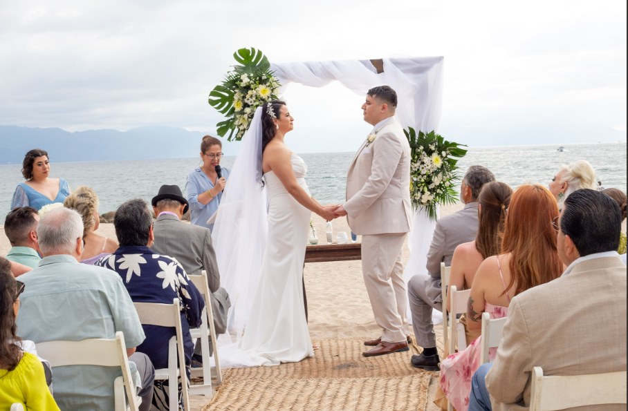 Beach ceremony with guests seated facing the ocean and a draped floral arch