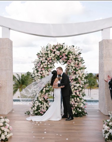 Couple kissing under a lush blush and white floral arch